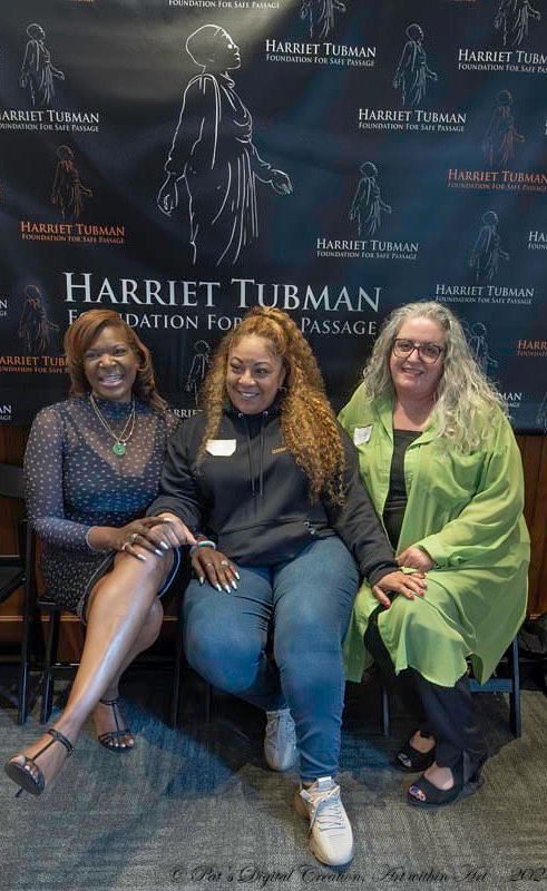 Three women sitting in front of a sign.