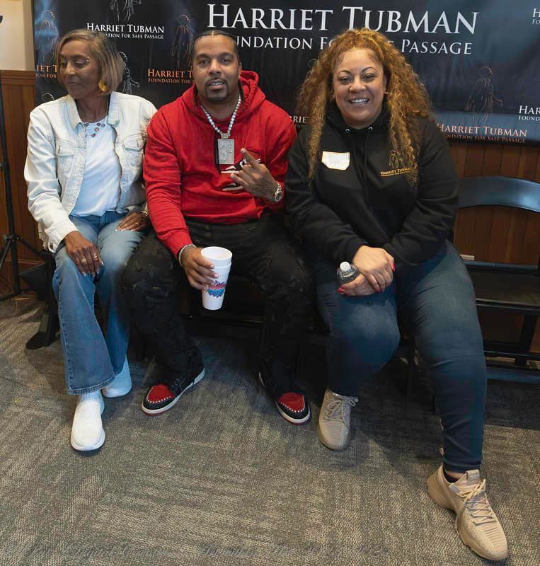 Three people sitting on a bench in front of a sign.